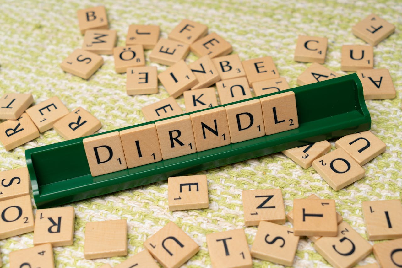 Home Scrabble tiles spelling 'dirndl' on a green tile holder with scattered letters on a textured surface.
