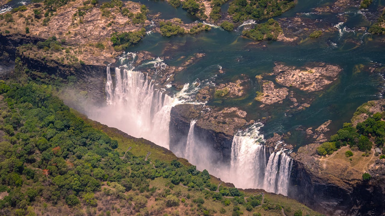 Services Breathtaking aerial view of Victoria Falls surrounded by lush greenery during summer day.