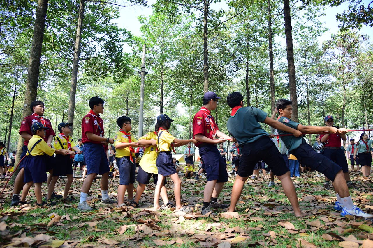 Services A group of children and adults engage in a tug of war competition during a scout camp in a forest setting.